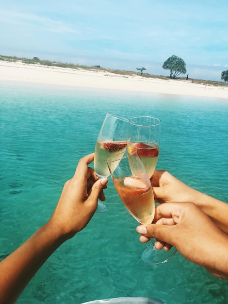 Photo cropped hands of people toasting drink in glasses over sea