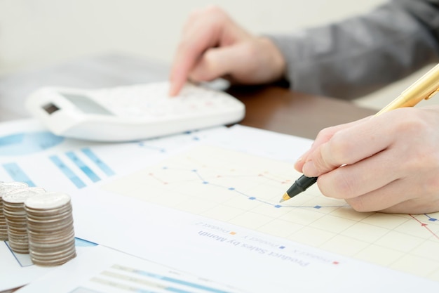 Cropped hands of person analyzing chart with calculator on table