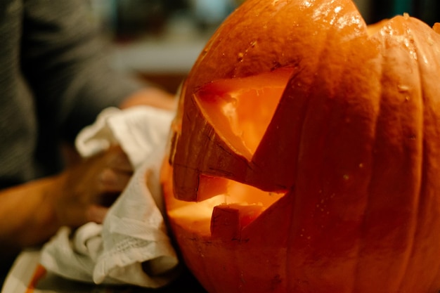 Photo cropped hands of person carving pumpkin on table at home