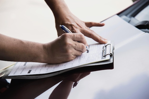 Cropped hands of person holding papers over car hood