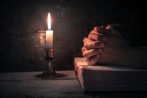 Cropped hands of person praying on bible and religious cross