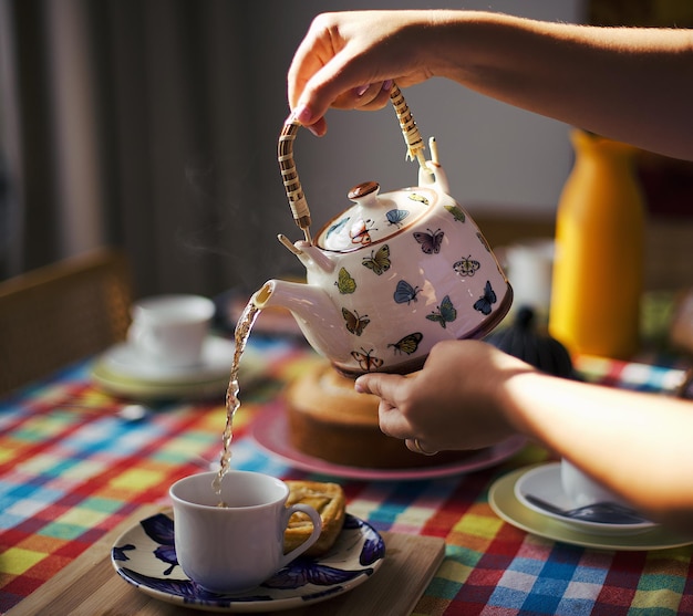 Foto mani tagliate che versano il tè in una tazza sul tavolo da pranzo a casa