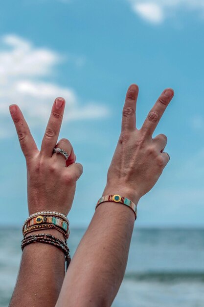 Photo cropped hands showing peace sign at beach against sky