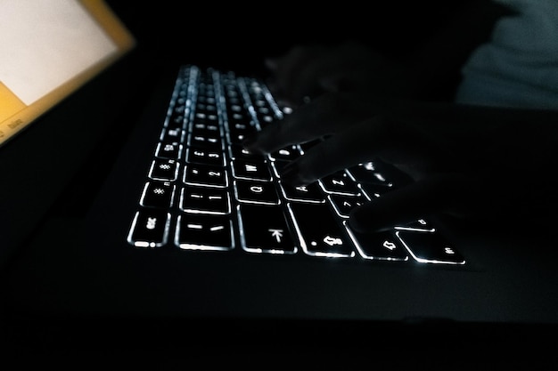 Photo cropped hands typing on illuminated keyboard