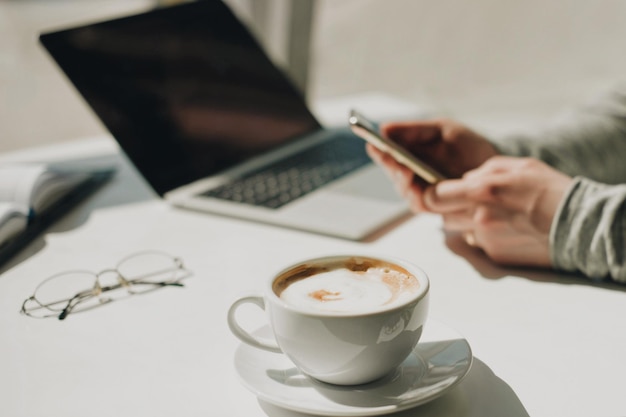 カフェのテーブルでコーヒーで携帯電話を使って手を切った