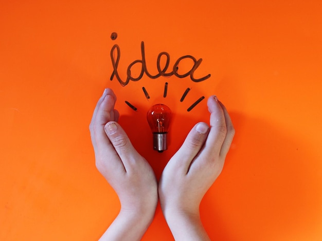 Photo cropped hands with light bulb and idea text on orange table