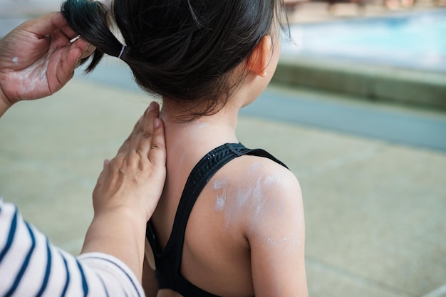 Cropped hands of woman applying suntan lotion on back of daughter at poolside