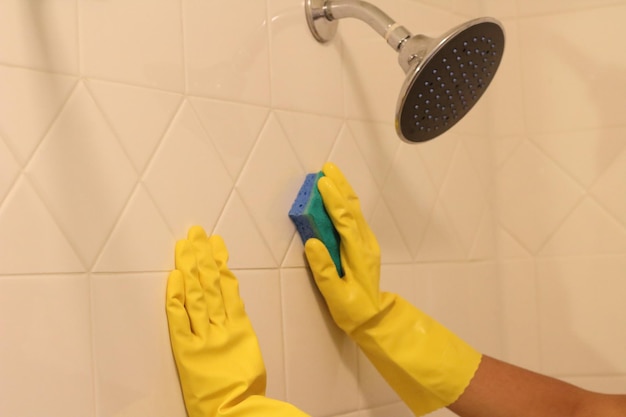 Photo cropped hands of woman cleaning wall in bathroom