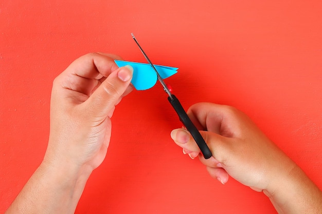 Cropped hands of woman cutting paper against red background