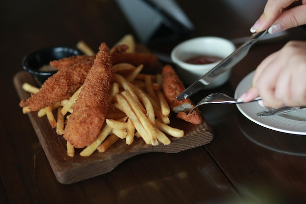 Foto mani tagliate di una donna che mangia pesce e patatine al tavolo di legno