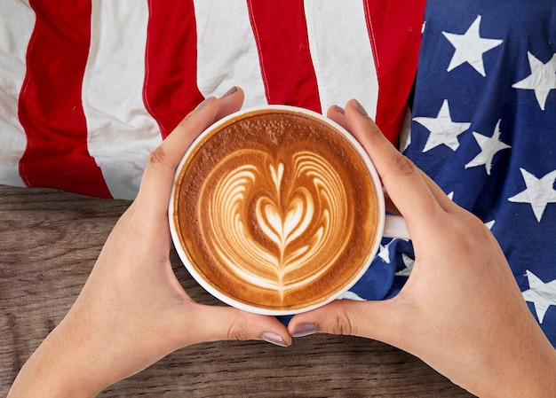 Photo cropped hands of woman holding coffee cup by american flag on table