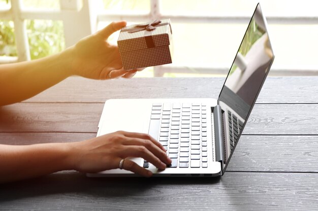 Cropped hands of woman holding gift and using laptop on table