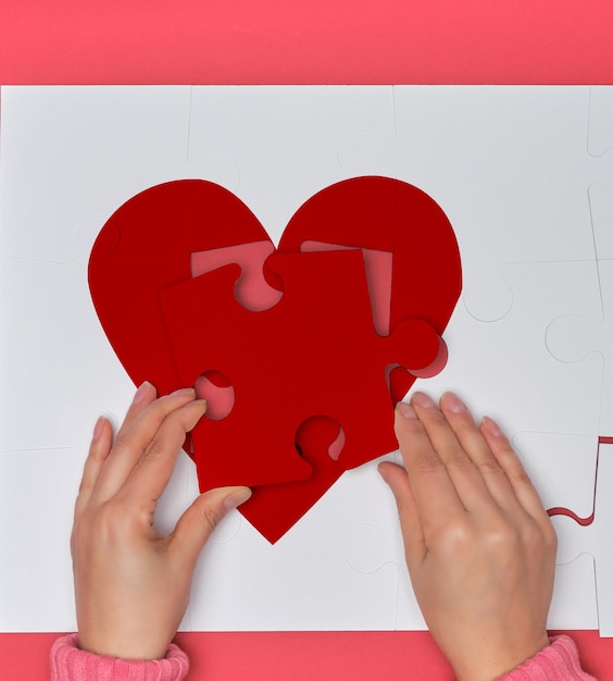 Cropped hands woman holding heart shape over jigsaw puzzle against pink background