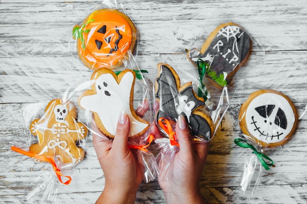 Photo cropped hands of woman holding various cookies wrapped in plastic over wooden table during halloween