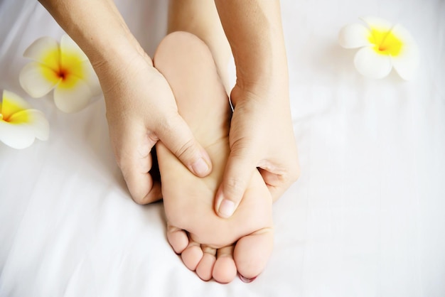 Cropped hands of woman massaging customer feet by flowers in spa