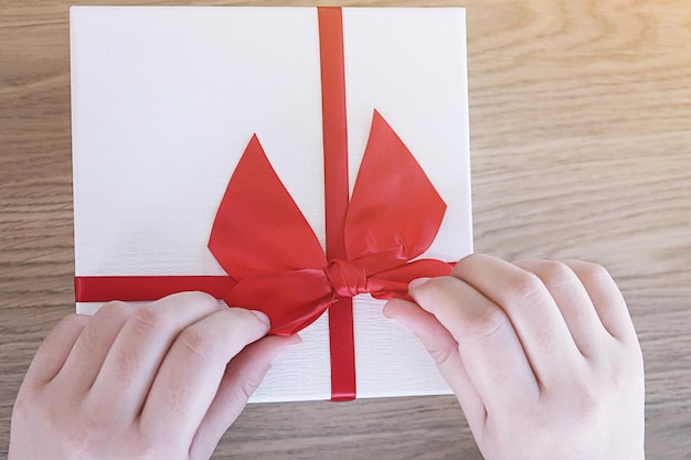 Foto mani tagliate di una donna che lega un nastro rosso su una scatola regalo