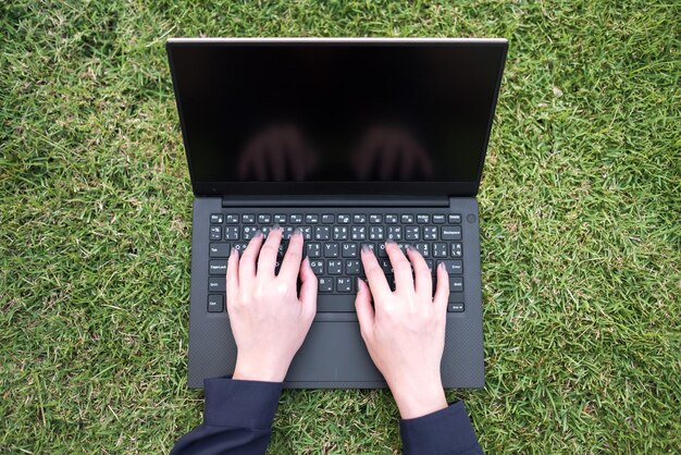 cropped hands of woman using laptop on grassy field