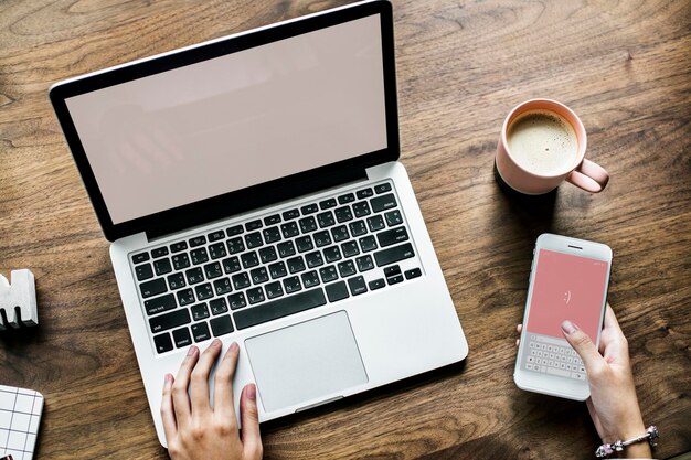 Photo cropped hands of woman using laptop and phone by coffee on table