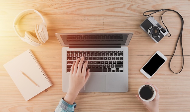 Cropped hands of woman using laptop on wooden table