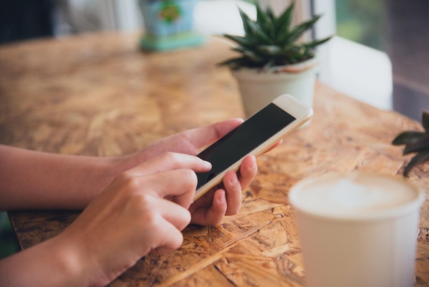 Photo cropped hands of woman using mobile phone at table in cafe