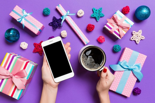 Cropped hands of woman using phone while having coffee amidst christmas decoration at table