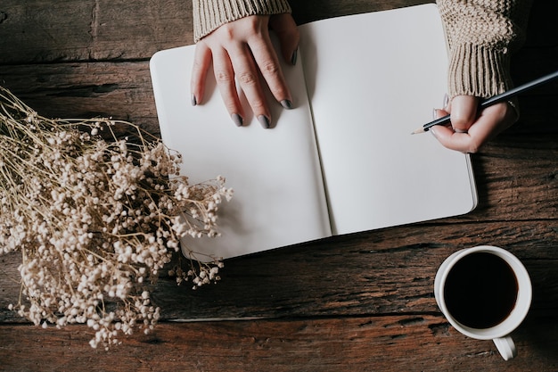 cropped hands of woman with book and pencil by black coffee on table