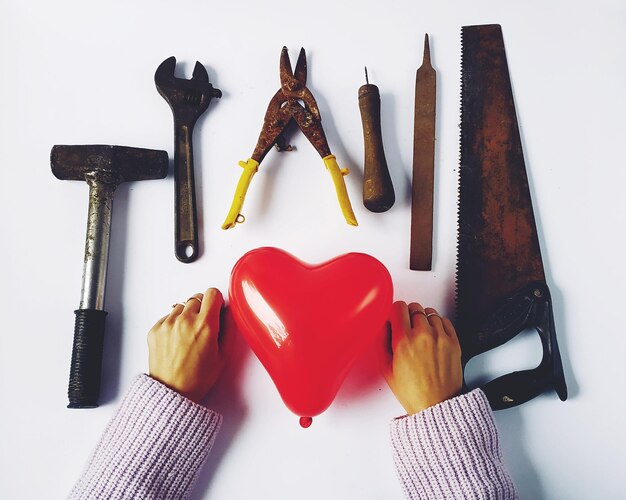 Photo cropped hands of woman with red heart shape balloon and work tools over white background