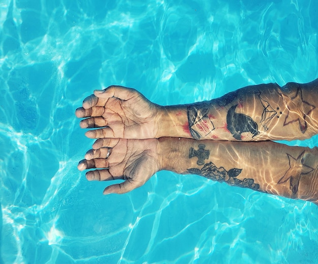 Cropped hands of woman with tattoos in swimming pool