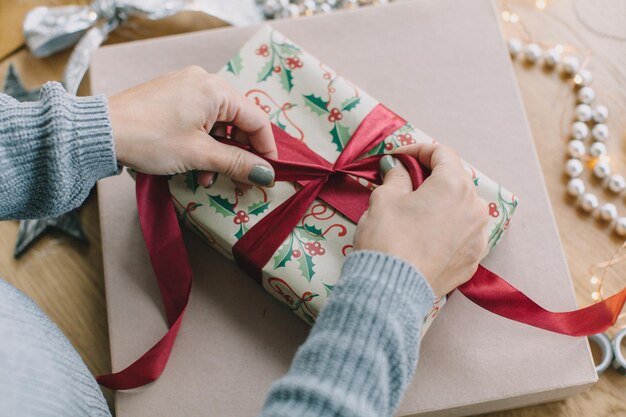 Photo cropped hands of woman wrapping gift on table at home