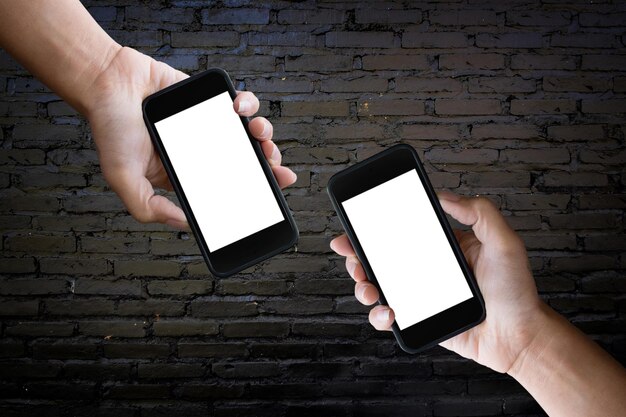 Cropped hands of women holding mobile phones against brick wall