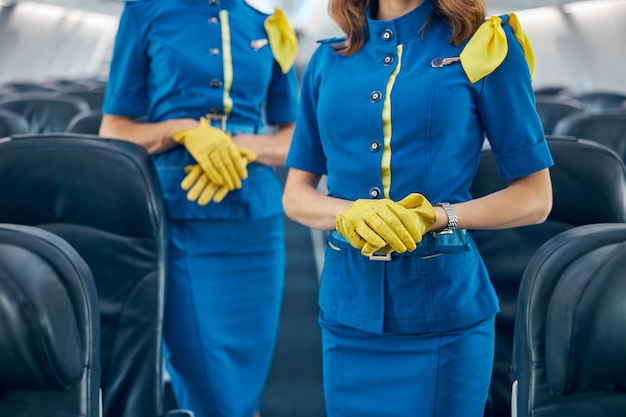 Cropped head portrait of females stewardesses keeping arms crossed while standing in modern salon of commercial airplane