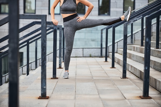 Cropped head of sporty female doing warm up of legs before workout on stairs outdoors