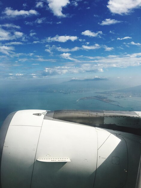 Photo cropped image of airplane against cloudy blue sky on sunny day