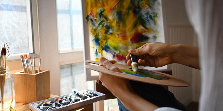 Photo cropped image of artist hands while holding and mixing oil color on artist palette over painting