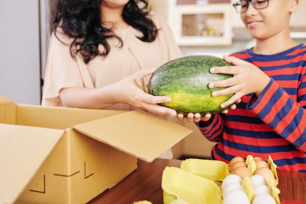 Cropped image of Asian mother and son taking fresh watermelon they ordered online out of cardboard box