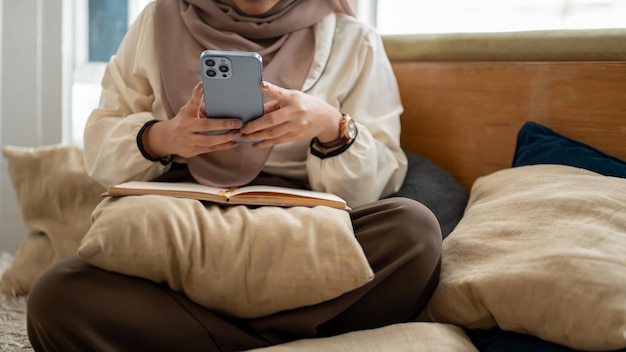 Photo cropped image of an asianmuslim woman using her smartphone while relaxing in a living room