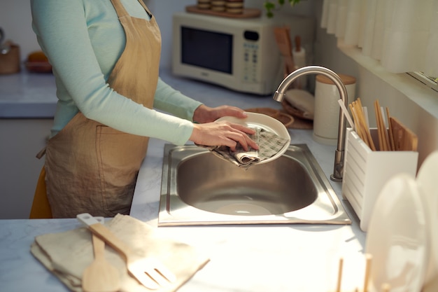 L'immagine ritagliata di una giovane donna attraente sta lavando i piatti mentre fa le pulizie a casa