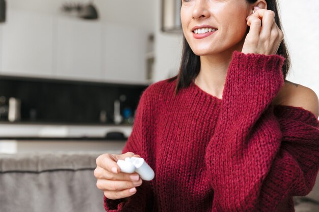 Cropped image of a beautiful woman indoors in home on sofa listening music with earphones.