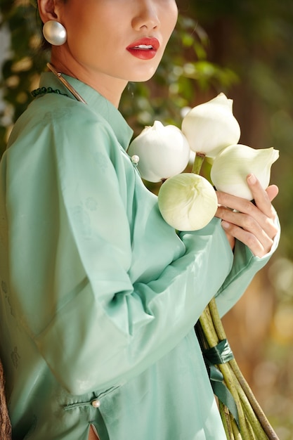 Photo cropped image of beautiful young woman standing outdoors with closed lotus flowers when standing in park