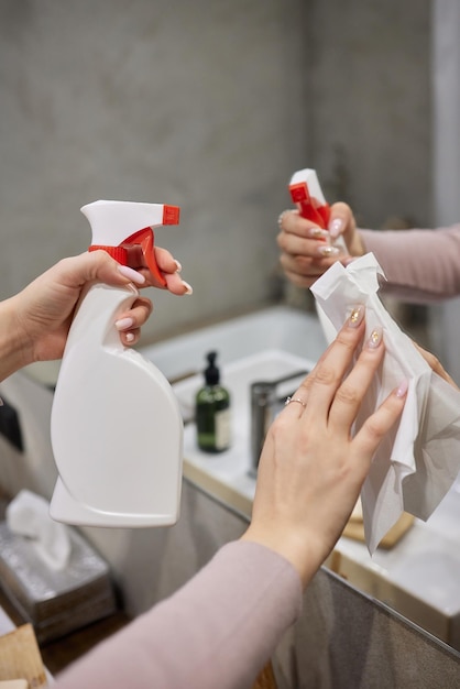 Cropped image of beautiful young woman using a duster and a detergent while cleaning sink and tap in bathroom