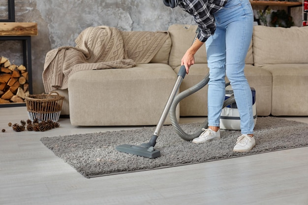 Cropped image of beautiful young woman using a vacuum cleaner while cleaning carpet in the house