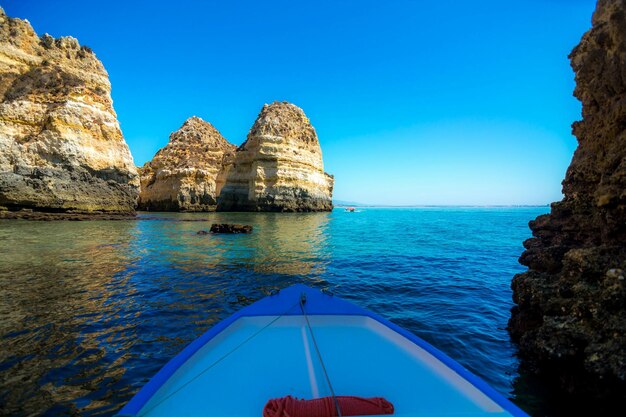 Foto immagine ritagliata di una barca che naviga sul mare vicino alle rocce contro un cielo blu limpido