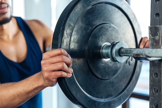Cropped image of a bodybuilder guy with barbell in a gym, keep barbell plate in hands