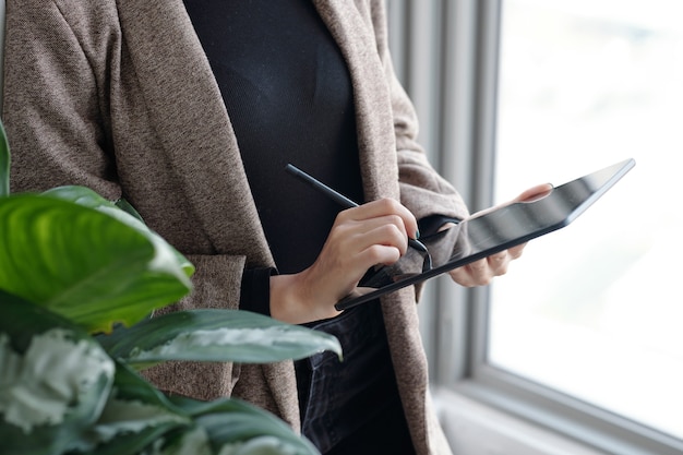 Cropped image of business lady filling document on tablet computer when standing at office window