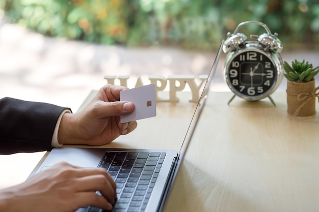 Photo cropped image of businessman holding credit card while using laptop at desk