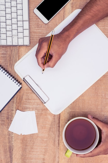 Cropped image of businessman writing on notebook at desk while holding coffee in office