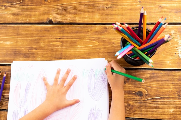 Photo cropped image of child drawing on paper by colored pencils at table