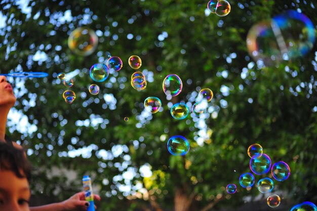 Foto immagine ritagliata di bambini che soffiano bolle contro un albero