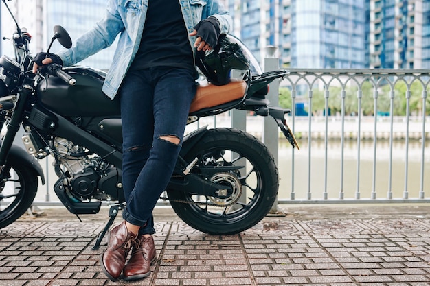 Cropped image of confident man in ripped jeans leaning on his motorcyclist