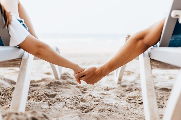 Cropped image of couple holding hands sitting at beach